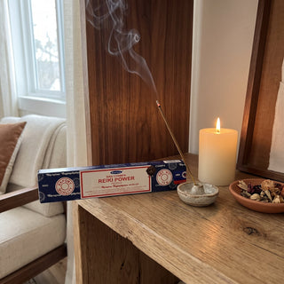 Reiki Power Satya Incense Sticks box displayed on a wooden home altar shelf beside a candle and a burning incense stick, shown at true size in warm light.