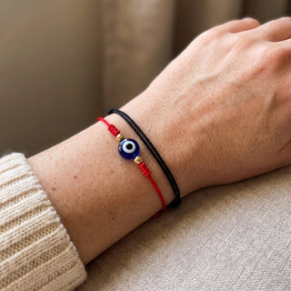 Evil Eye Bracelet with Adjustable Cord 2 Pack worn on a wrist in natural light, showing the red-cord and black-cord string bracelets with blue evil-eye charms at true scale.