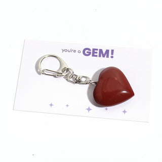 One of the five deep red jasper heart charms from the pack, shown on its "you're a GEM!" gift backing card, hanging from its silver clasp on a clean white background. Stonebridge Imports.