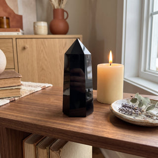 Black Obsidian Generator Unique #15 displayed on a wooden home altar shelf beside a lit candle and dried botanicals, shown at true size in warm natural light.