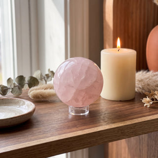 Rose Quartz Sphere Unique #192 displayed on a wooden home altar shelf beside a candle, the 3 inch pink sphere shown at true size in warm natural light.