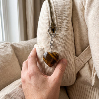 One of the five golden-brown tiger eye heart charms from the pack, clipped to a knit backpack zip in natural light, shown at true scale.