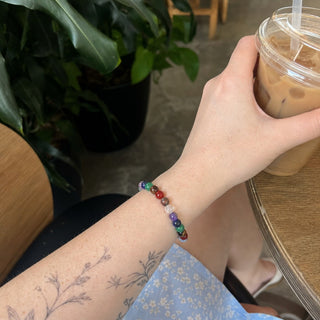 Seven Chakra bead bracelet worn on a tattooed forearm holding a coffee