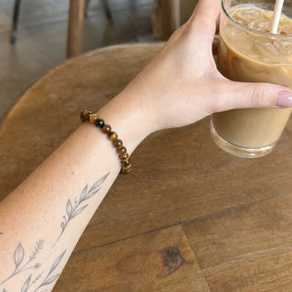 Gold Tiger's Eye bead bracelet worn on a tattooed forearm holding a coffee