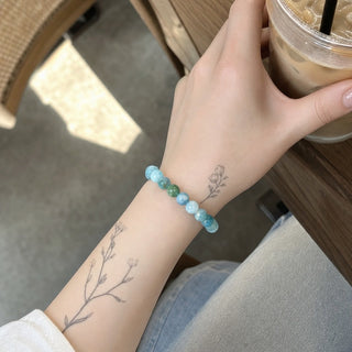 Hemimorphite bead bracelet worn on a tattooed forearm holding a coffee