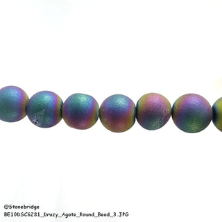 A horizontal strand of round rainbow electroplated druzy agate beads displays shimmering purple, blue, and green hues against a plain white background. Stonebridge Imports.