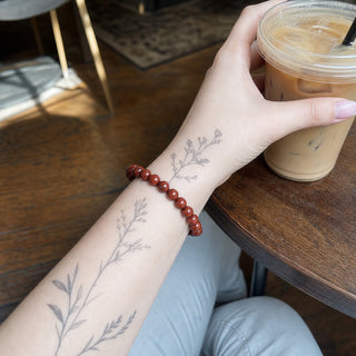 Red Jasper bead bracelet worn on a tattooed forearm holding a coffee