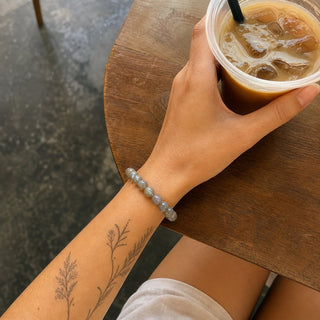 Labradorite bead bracelet worn on a tattooed forearm holding a coffee