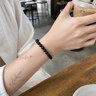 Black Onyx bead bracelet worn on a tattooed forearm holding a coffee