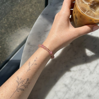 Strawberry Quartz bead bracelet worn on a tattooed forearm holding a coffee