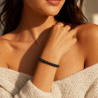 Shungite bead bracelet worn with the fingertips resting at the collarbone
