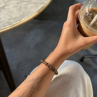 Smoky Quartz bead bracelet worn on a tattooed forearm holding a coffee