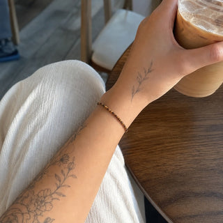 Tiger's Eye bead bracelet worn on a tattooed forearm holding a coffee